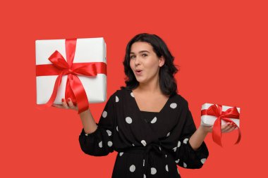 Siyah elbiseli gülümseyen kadın kırmızı kurdeleli küçük ve büyük Noel hediyeleri arasında seçim yapıyor.