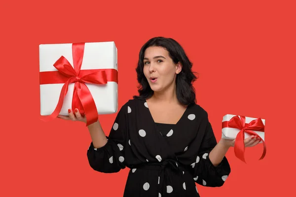 Usmívající se žena v černých šatech výběru mezi malými a velkými vánoční dárkové krabice s červenou stuhou — Stock fotografie