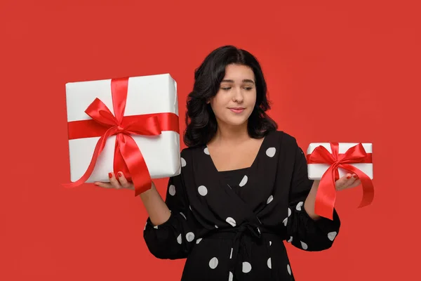 Usmívající se žena v černých šatech výběru mezi malými a velkými vánoční dárkové krabice s červenou stuhou — Stock fotografie