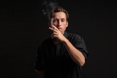 Sigara içen şık genç adam. Dramatik atmosfer, siyah arkaplan