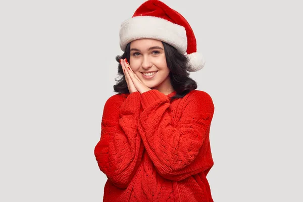 漂亮的黑发姑娘，穿着红色毛衣，头戴一顶灰色背景的圣诞老人帽. — 图库照片