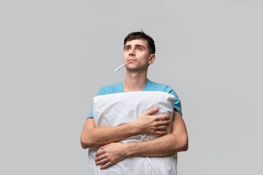 Genç esmer adam yastığa sarılıyor ve sıcaklığı ölçüyor..