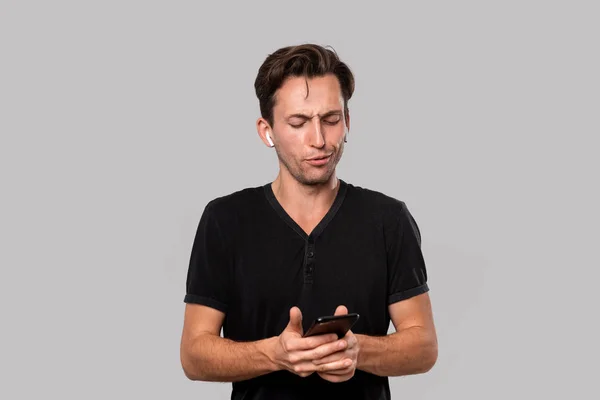 Young handsome man with wireless earbuds looking at the screen of a smartphone. — Stock Photo, Image