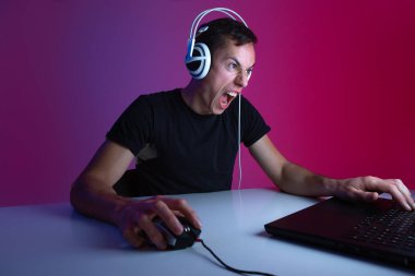 Karanlık bir odada neon ışıklarla aydınlatılmış, bilgisayar başında video oyunu oynayan, kulaklık takan kızgın bir oyuncu..