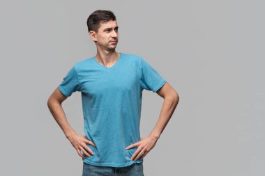 Mavi tişörtlü kendine güvenen bir adam el ele tutuşup kalçalarına bakıyor. Güven kavramı.