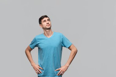 Mavi tişörtlü kendine güvenen bir adam el ele tutuşup kalçalarına bakıyor. Güven kavramı.