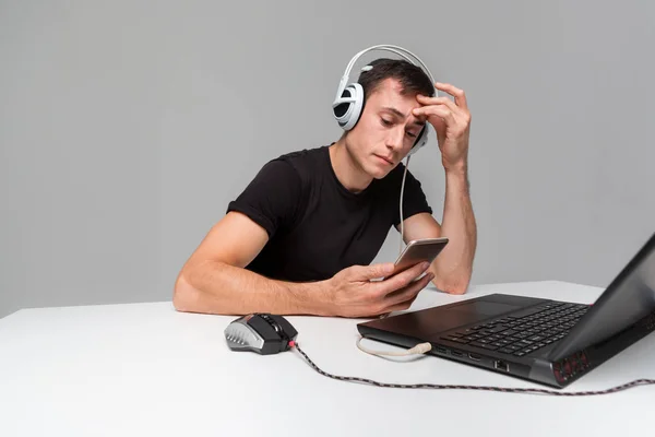 Gamer wearing headphones checking smartphone while playing video games on computer.