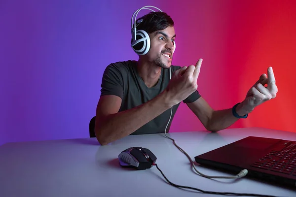 Retrato de un jugador enojado jugando videojuegos en la computadora en la habitación oscura con auriculares . —  Fotos de Stock