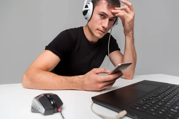 Gamer wearing headphones checking smartphone while playing video games on computer.