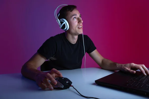 Pensativo jugador en auriculares tomar un descanso durante el videojuego en una habitación oscura iluminada con luces de neón —  Fotos de Stock