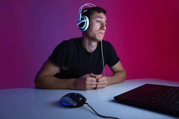 Gamer con auriculares jugando videojuegos en el ordenador en una habitación oscura iluminada con luces de neón . —  Fotos de Stock