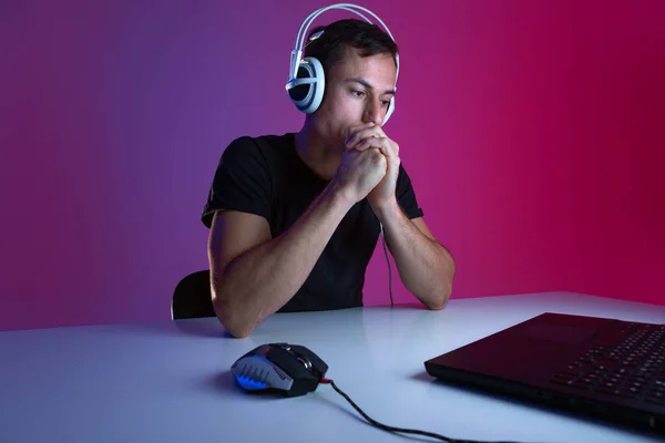 Gamer molesto usando auriculares jugando videojuegos en la computadora en una habitación oscura iluminada con luces de neón . —  Fotos de Stock