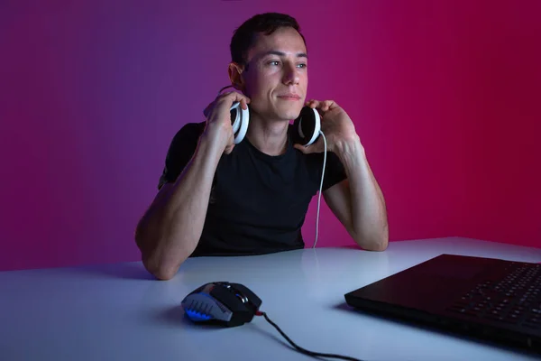 Gracz nosi słuchawki grając w gry wideo na komputerze w ciemnym pokoju oświetlonym światłami neonowymi. — Zdjęcie stockowe