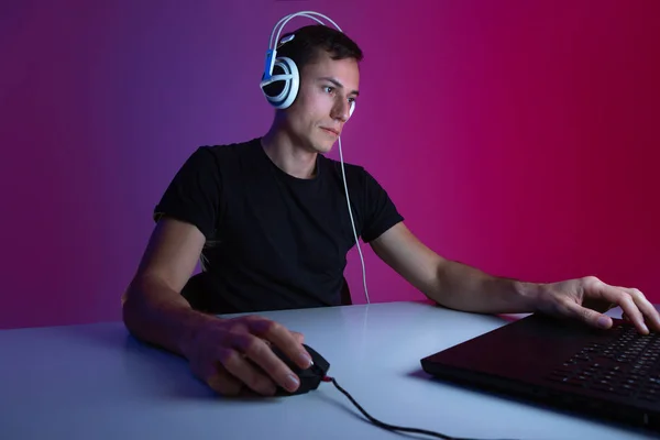 Gamer con auriculares jugando videojuegos en el ordenador en una habitación oscura iluminada con luces de neón . —  Fotos de Stock