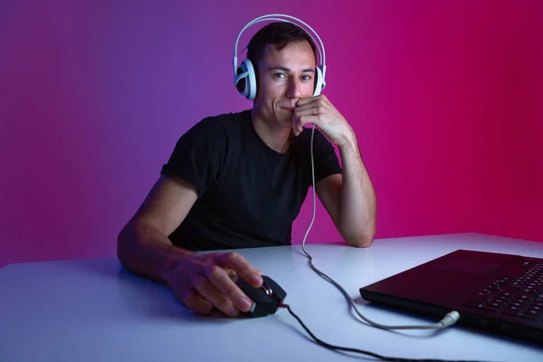 Gamer con auriculares jugando videojuegos en el ordenador en una habitación oscura iluminada con luces de neón . —  Fotos de Stock