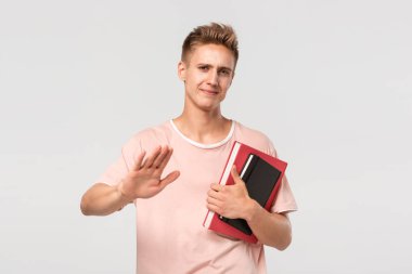 Elinde kitap ve dosyalar olan pembe tişörtlü yakışıklı genç adam dur işareti gösteriyor.
