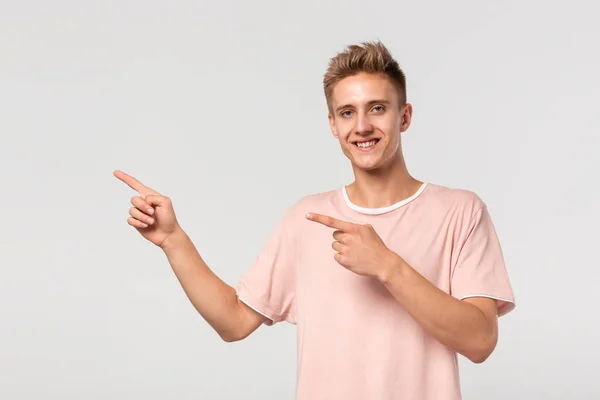 Stilig ung man i rosa tee visar med fingrarna kvar på tomrummet för reklam. — Stockfoto