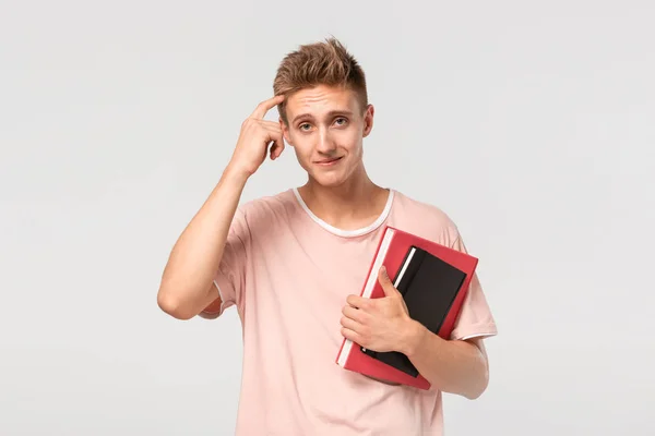 Jovem bonito com livros e arquivos apontando com o dedo na cabeça — Fotografia de Stock