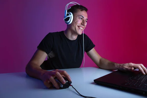 Kulaklıklı oyuncu, karanlık bir odada neon ışıklarla aydınlatılmış bilgisayarda video oyunları oynuyor..