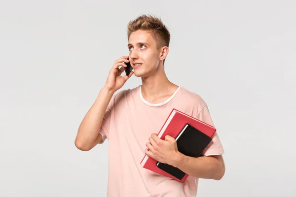 一个穿着粉色T恤、拿着书本和文件在电话里聊天的英俊年轻人. — 图库照片