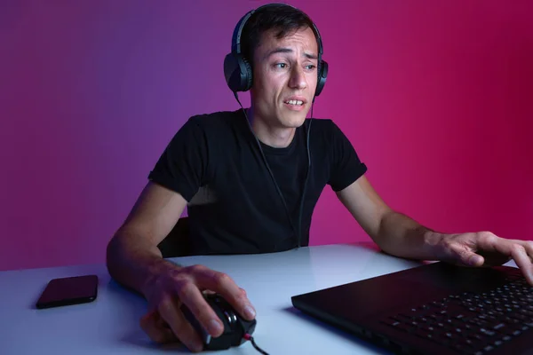 Gracz w słuchawkach grający w gry wideo na komputerze w ciemnym pokoju oświetlonym światłami neonowymi. — Zdjęcie stockowe