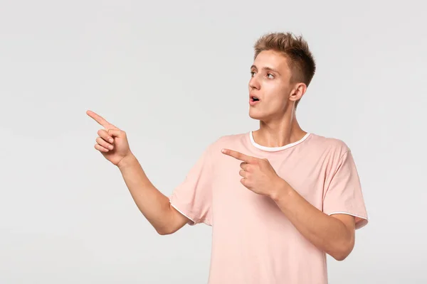 Przystojny młody człowiek w różowej koszulce pokazuje z palcami w pustej przestrzeni na reklamę. — Zdjęcie stockowe