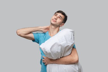 Genç esmer adam gri arka planda beyaz yastık tutarak rüya görüyor. Uyku kavramı.
