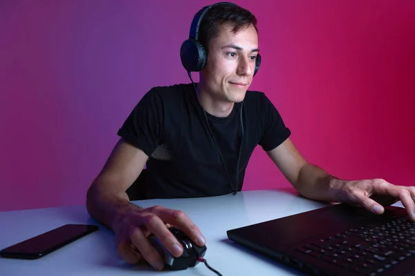 Gracz nosi słuchawki grając w gry wideo na komputerze w ciemnym pokoju oświetlonym światłami neonowymi. — Zdjęcie stockowe