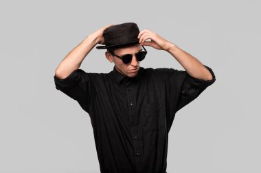 Tarz sahibi yakışıklı bir adam. Gri arka planda siyah bir gömlek ve domuz pastası şapkası.