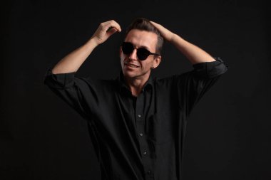 Siyah gözlüklü, kendine güvenen, siyah arka planda izole edilmiş saçları tamir eden şık bir adam..