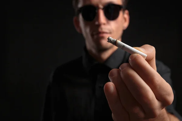 Крупный план стильного молодого человека в черной футболке и солнцезащитных очках с сигаретой — стоковое фото