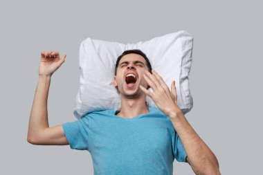 Gri arka planda izole edilmiş beyaz yastıkta dinlenen mavi tişörtlü yorgun esmer adam..