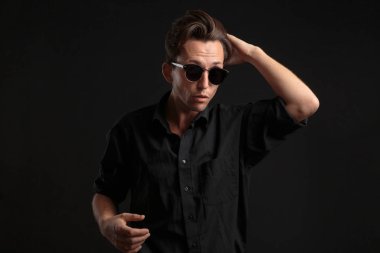 Siyah gözlüklü, kendine güvenen, siyah arka planda izole edilmiş saçları tamir eden şık bir adam..