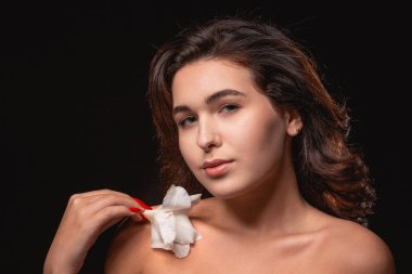 Parlak makyajlı güzel bir kadın siyah arka planda beyaz çiçekle yalnız poz veriyor..