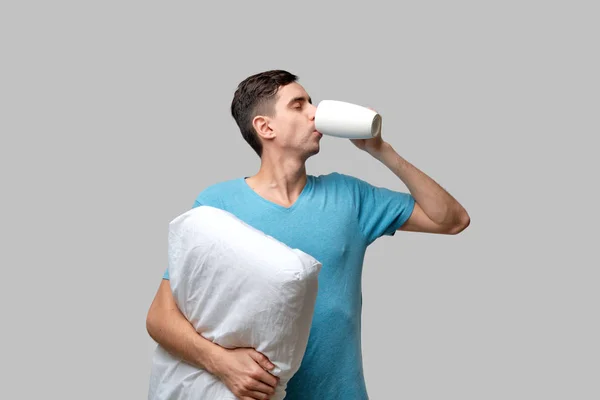 Pemuda brunet minum kopi bentuk cangkir putih memegang bantal putih — Stok Foto