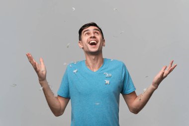 Mavi tişörtlü yakışıklı adam başparmağıyla gülümsüyor çünkü yastığın tüyü etrafında uçuşuyor.