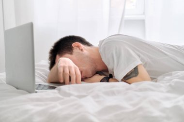 Beyaz çarşaflı beyaz gömlekli genç adam dizüstü bilgisayara bakarken üzgün..