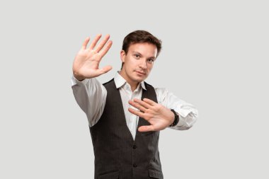 Confindent handsome man in a white shirt and grey vest expressing Stop gesture