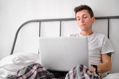 Beyaz çarşaflı beyaz gömlekli genç adam dizüstü bilgisayara bakarken üzgün..
