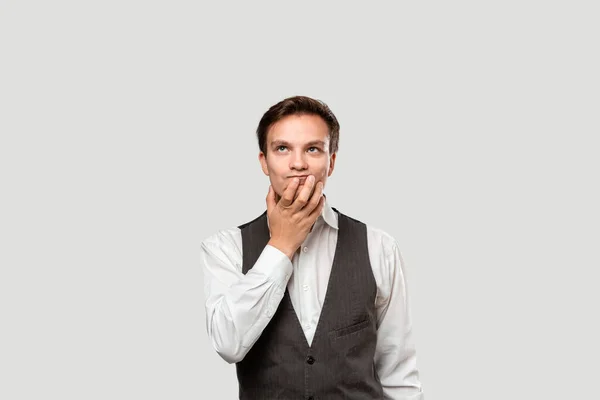 Pensativo joven hombre de negocios con una camisa blanca y chaleco gris sosteniendo la barbilla en una palma de una mano — Foto de Stock