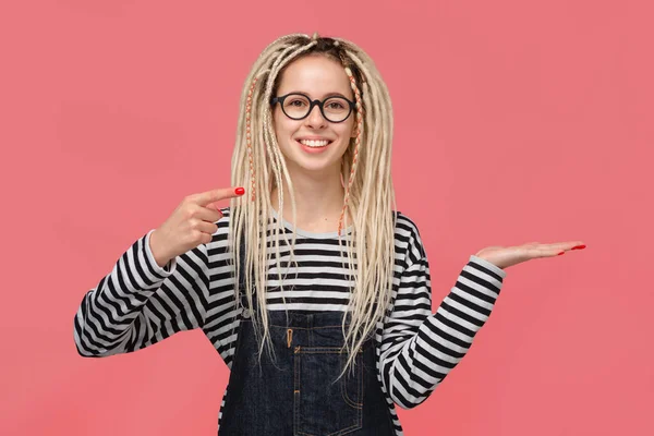 Girl with dreads in a striped shirt and jeans jumpsuit pointing at copy space on a palm of a hand — ストック写真