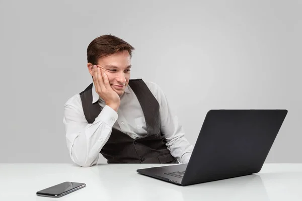 Empresário em uma camiseta branca e colete cinza está entediado e olhando para a tela de um laptop — Fotografia de Stock
