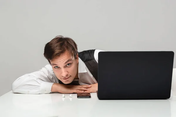 Empresario en una camiseta blanca y chaleco gris se esconde detrás de la computadora portátil . — Foto de Stock