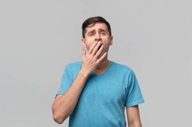 Mavi tişörtlü yakışıklı adam esniyor. Etrafında uçuşan bir yastıktan tüy.