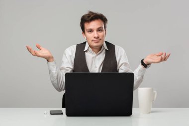 Utangaç adam, beyaz masada oturan kameraya bakarak omuz silkip cevap vermiyor.