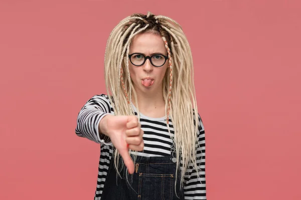 Young girl with dreadlocks in a striped shirt and jeans jumpsuit is upset holding thumbs down. — 스톡 사진