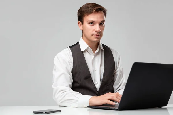 Empresario con camiseta blanca y chaleco gris trabajando en un portátil. Hombre mirando a la cámara — Foto de Stock