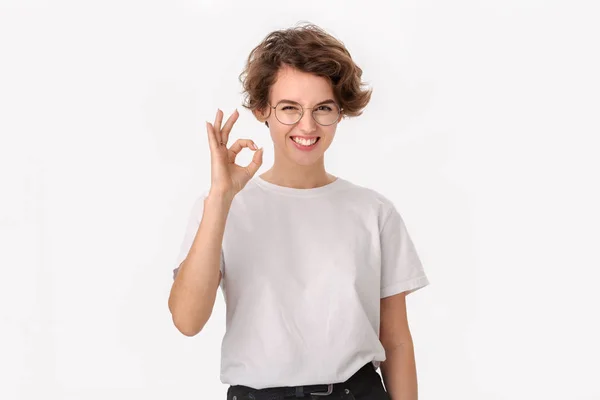 Mujer bastante sonriente en una camisa blanca y gafas que muestran signo OK para expresar aprecio — Foto de Stock