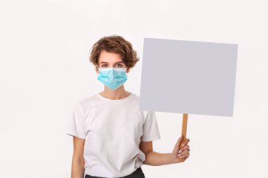 Worried woman wearing blue medical mask holds picket sign with copy space and piniting at her head