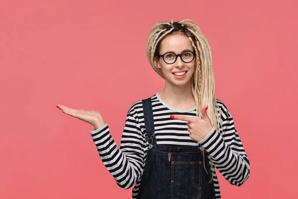 Girl with dreads in a striped shirt and jeans jumpsuit pointing at copy space on a palm of a hand — ストック写真